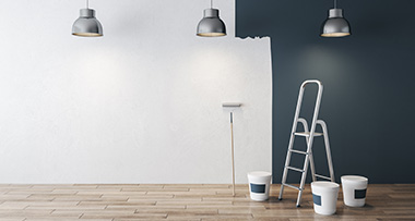 a wall half painted with dark paint, with paint buckets, a roller and a step ladder in front