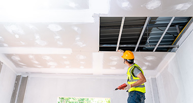 a worker with a safety helmet installing dry wall onto a ceiling