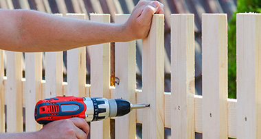 a person holding an installed fence with one hand and using a drill to secure it with another