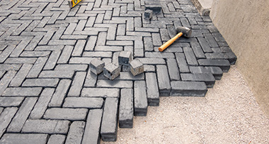 a driveway in the middle of being installed with black bricks, with a hammer and off-cuts on top