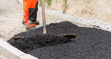 a person using a broom to spread tarmac around a path