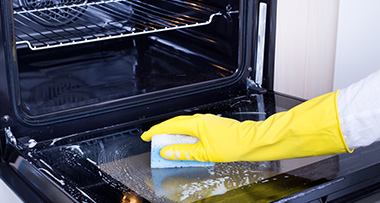 a person with a yellow rubber glove cleaning an oven 