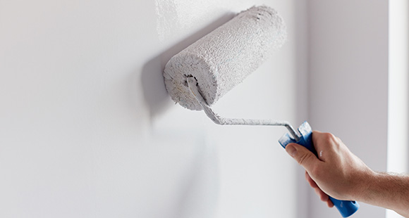 a person using a paint roller to paint a wall white