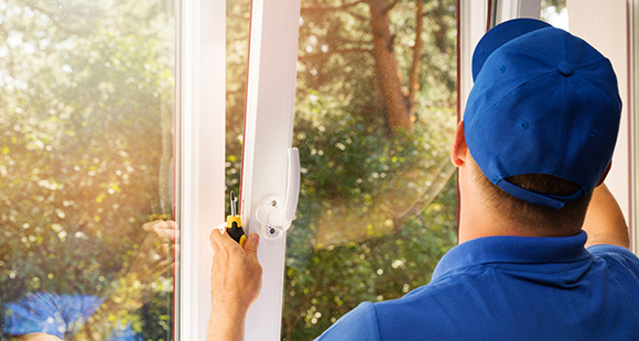 a man wearing a blue uniform installing a window while holding a screwdriver