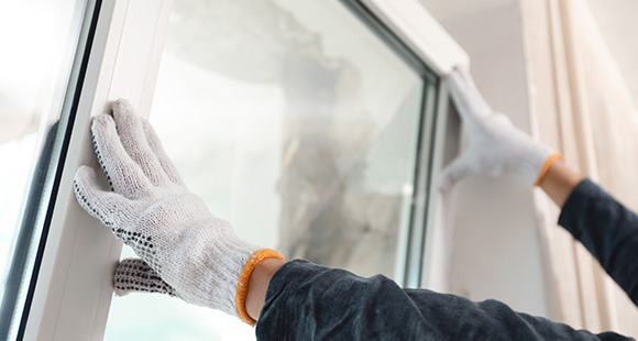 a person wearing gloves pushing a window into place for installation