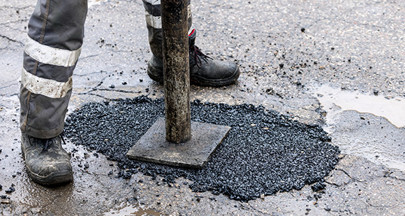 a person stamping down tar into a pothole for a repair