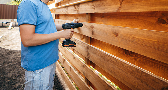 a man installing a wooden fence in a garden using an electric drill